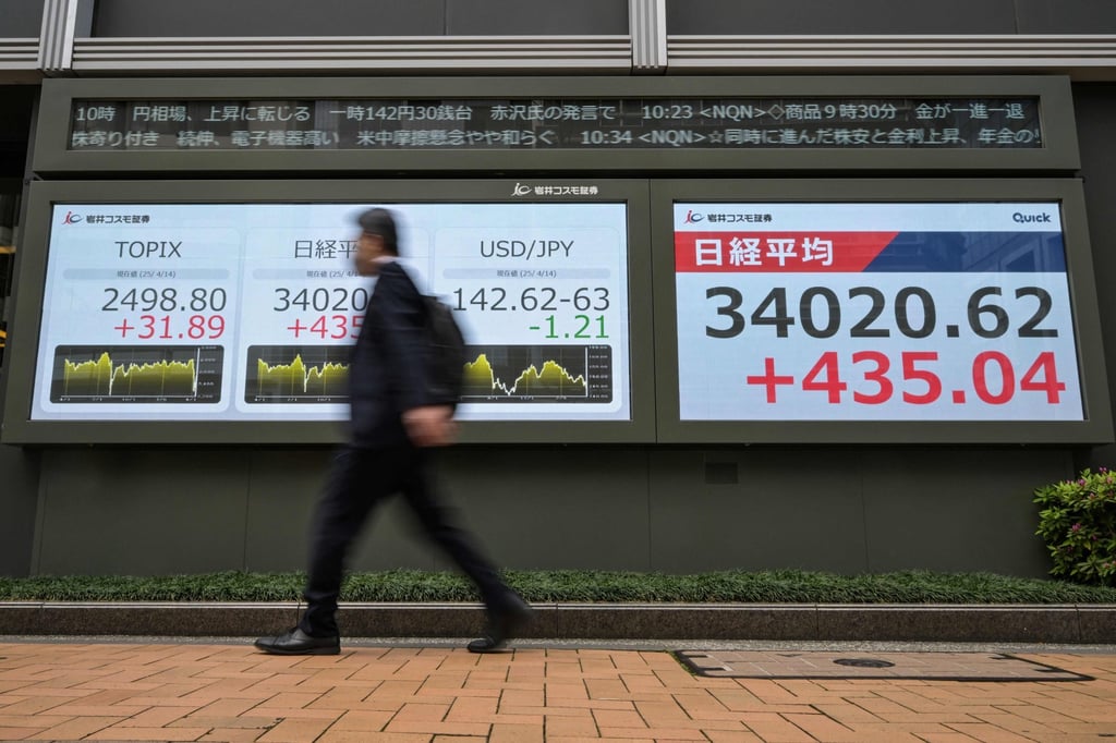 A man in Tokyo, Japan, walks past an electronic board showing the Japanese yen and US dollar exchange rate (centre), and the morning trading of the Tokyo Stock Exchange (right) on April 14. Photo: AFP