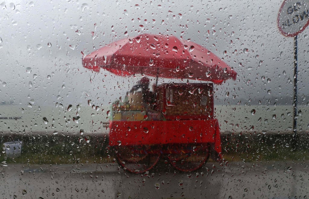 epa12307903 A photo taken from the windscreen of a car shows a roadside vendor waiting for customers during rainfall in Srinagar, India, earlier this month. Photo: EPA