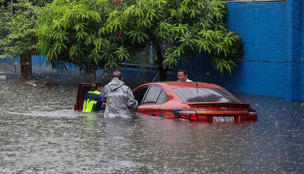 People push a car that has been partially submerged in floodwater during heavy rain in Quezon City on Saturday. Photo: Xinhua