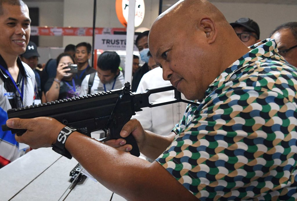Senator Dela Rosa tries a semi-automatic rifle during a defence and sporting show in May 2023. Photo: AFP