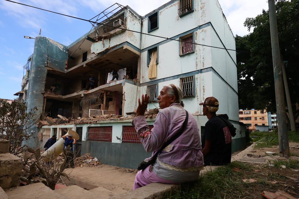 Two people sit in front of a building in La Guaira, Venezuela, that was destroyed in a US bombing raid, as others remove rubble, on January 4. Photo: dpa