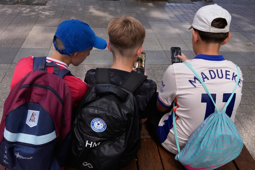 Three boys use their phones while sitting outside a school in Sydney in 2025. Photo: AP