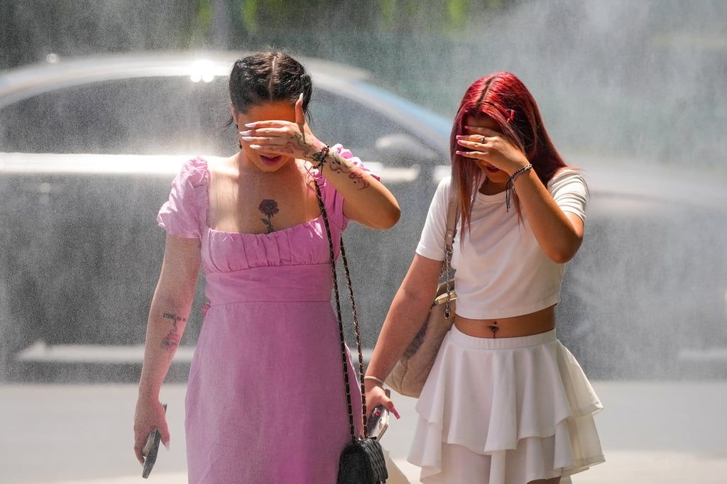 People walk by a water mist machine in Romania’s city of Bucharest. The machine was installed by officials to help with coping in the heat. Photo: AP