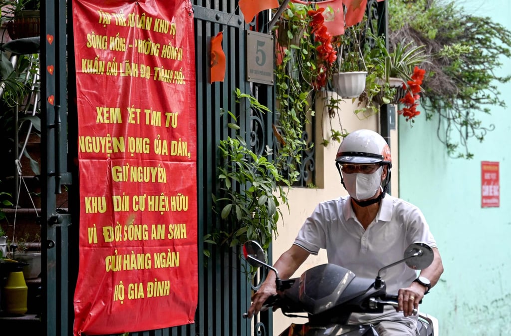 A man rides a motorcycle past a banner protesting a massive redevelopment scheme that could displace hundreds of thousands in Hanoi on June 19. Photo: AFP