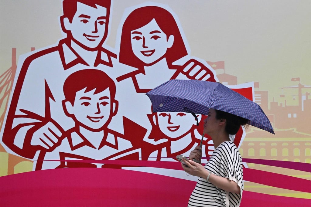 A pregnant woman holding an umbrella walks past a billboard in Hanoi showing a happy family last month. Photo: AFP