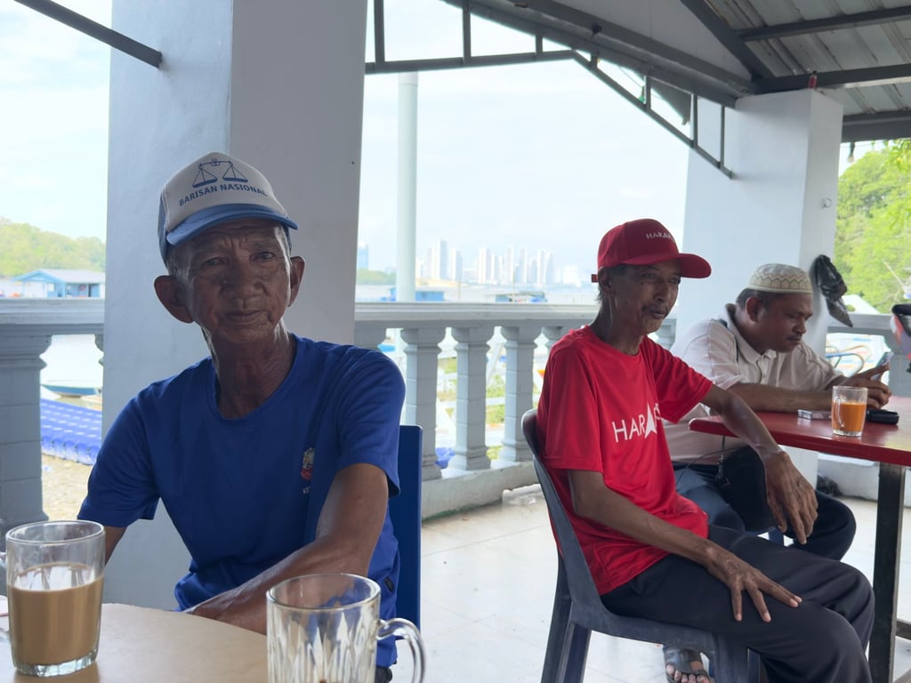 A Barisan Nasional supporter sits beside a Pakatan Harapan fan at a local shop in Kampung Sungai Melayu, Iskandar Puteri, on the eve of Johor’s state election in Malaysia. Photo: Iman Muttaqin Yusof
