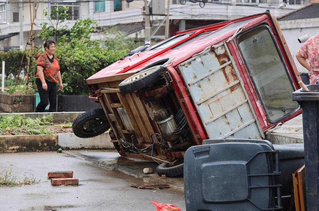 A woman walks past a vehicle knocked over by winds from Typhoon Bavi in Wenling, in China’s eastern Zhejiang province on July 12, 2026. Photo: AFP
