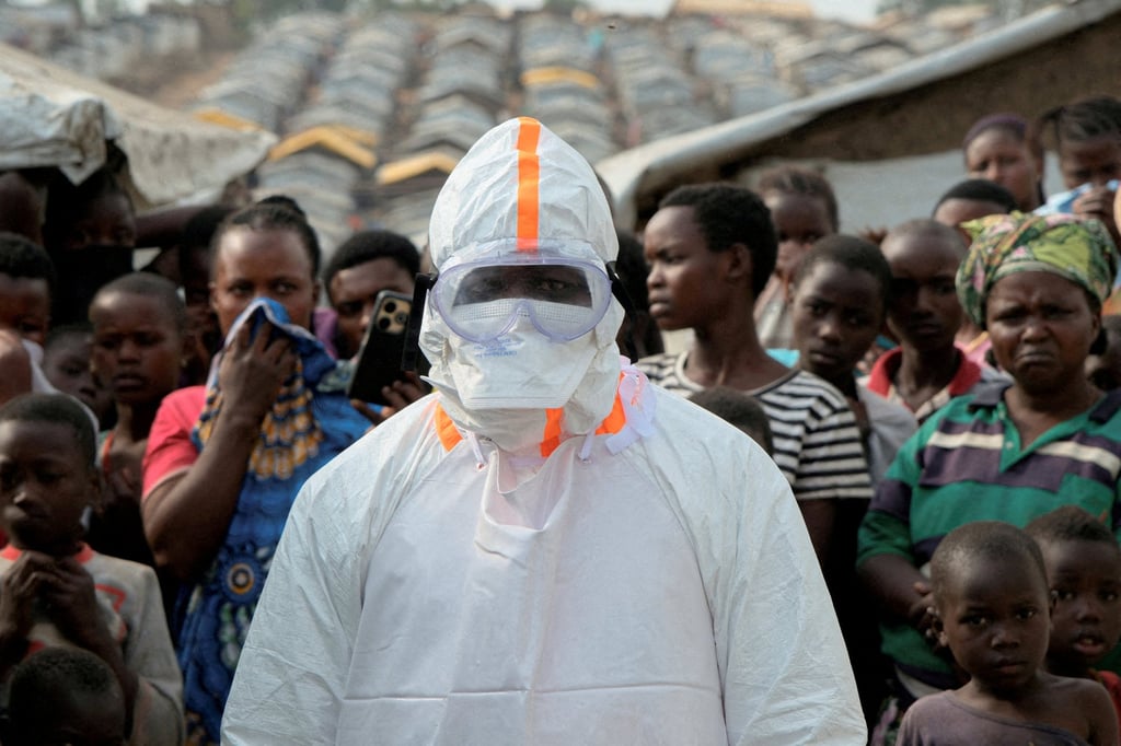 A health worker in personal protective equipment stands near displaced people waiting for the burial of suspected Ebola victims at the Kigonze displaced persons camp in the Republic of the Congo last month. Photo: Reuters