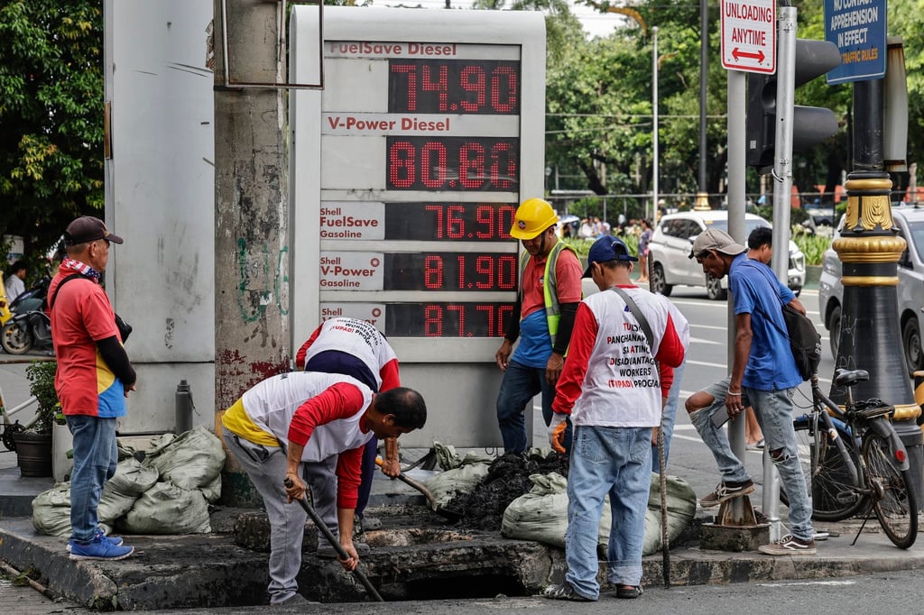 Workers declog a drainage canal beside a petrol station displaying fuel prices in Manila, the Philippines, on Monday. Photo: EPA