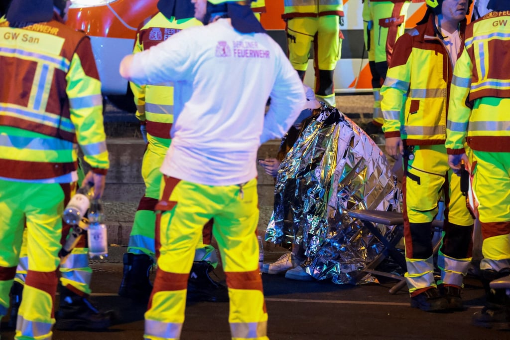 A person sits wrapped in a thermal blanket, as emergency responders work at the site of a deadly crash in Berlin on Saturday. Photo: Reuters