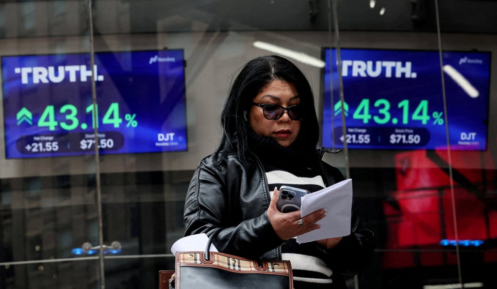 A woman looks at her phone in front of screens displaying trading information about shares of Truth Social and Trump Media & Technology Group outside the Nasdaq Market site in New York on March 26, 2024. Photo: Reuters