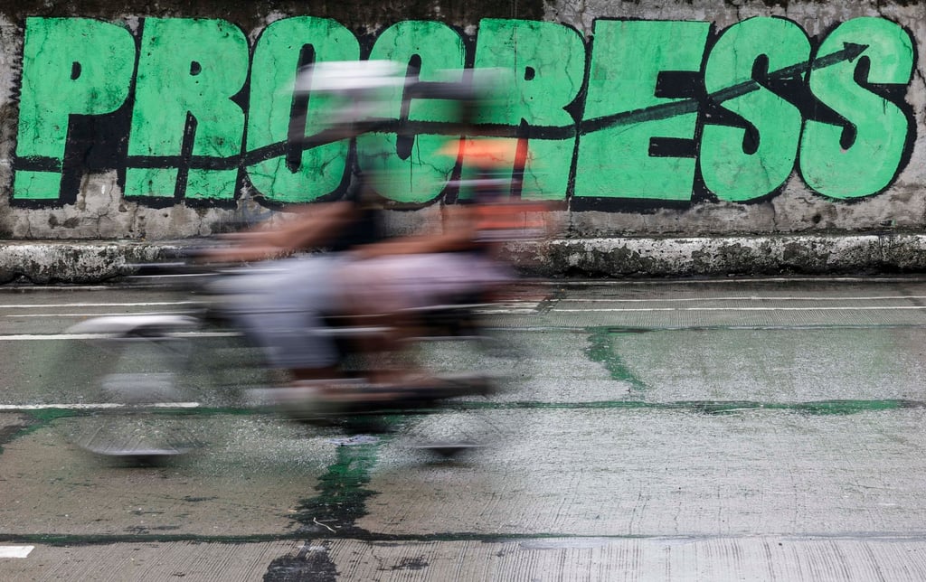 People ride a motorcycle past graffiti that reads, “Progress” in Quezon City, Metro Manila, on Monday. Initial Metro Manila investments could later lead to expansion in other parts of the country, said Tereso Panga, Peza’s director general. Photo: EPA
