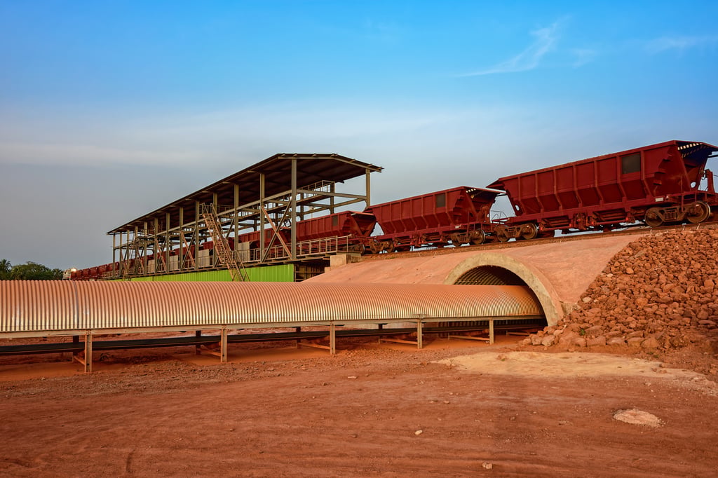 A goods train carrying bauxite for transshipment into bulk carrier ships by covered conveyor belt mechanism, in the Kamsar, Guinea. Photo: Shutterstock