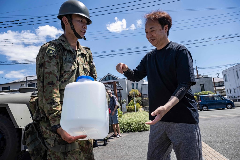A member of Japan’s Self-Defence Forces hands a water container to a man at a water distribution station following the July 28 earthquake in Kumamoto prefecture. Photo: AFP