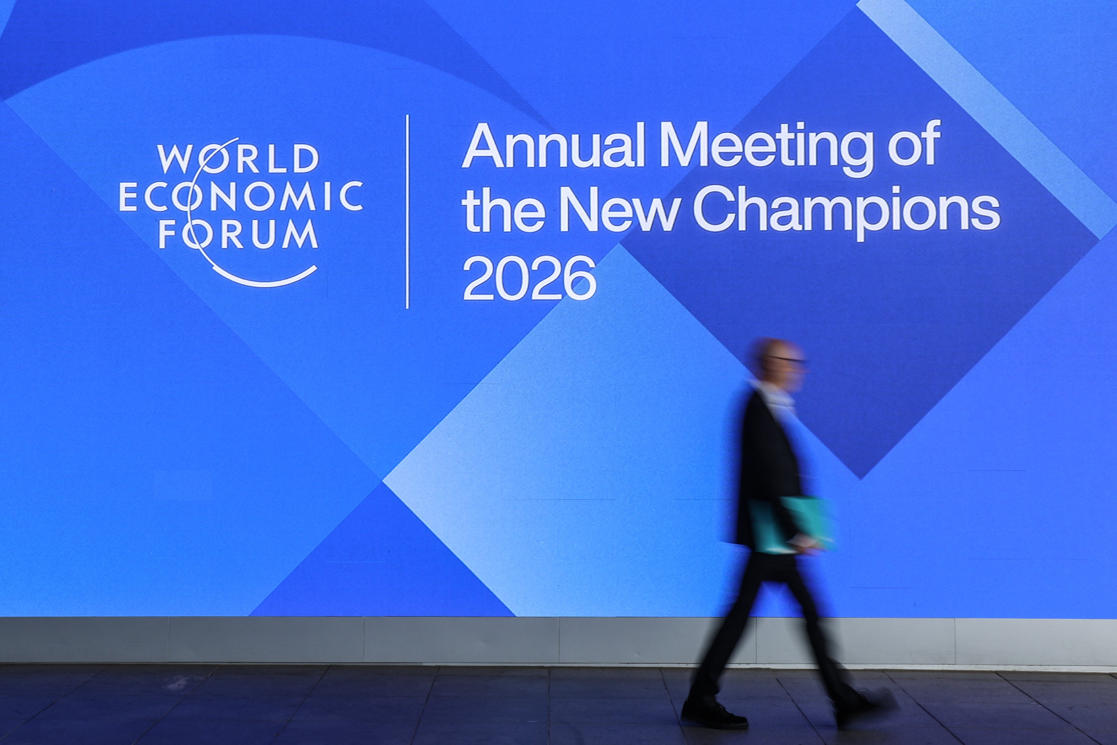 A participant passes a billboard for the Annual Meeting of the New Champions in Dalian. Photo: Xinhua