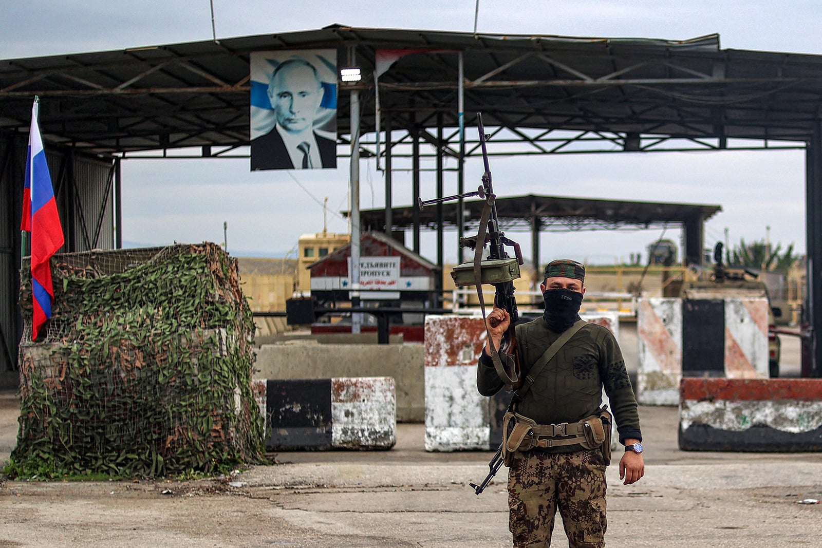 A Syrian rebel fighter stands at an inspection checkpoint for incoming vehicles before a Russian flag and Russian soldiers behind manning the entrance of the Russian-leased Syrian military base of Hmeimim in Latakia province in Syria in 2024. Photo: TNS