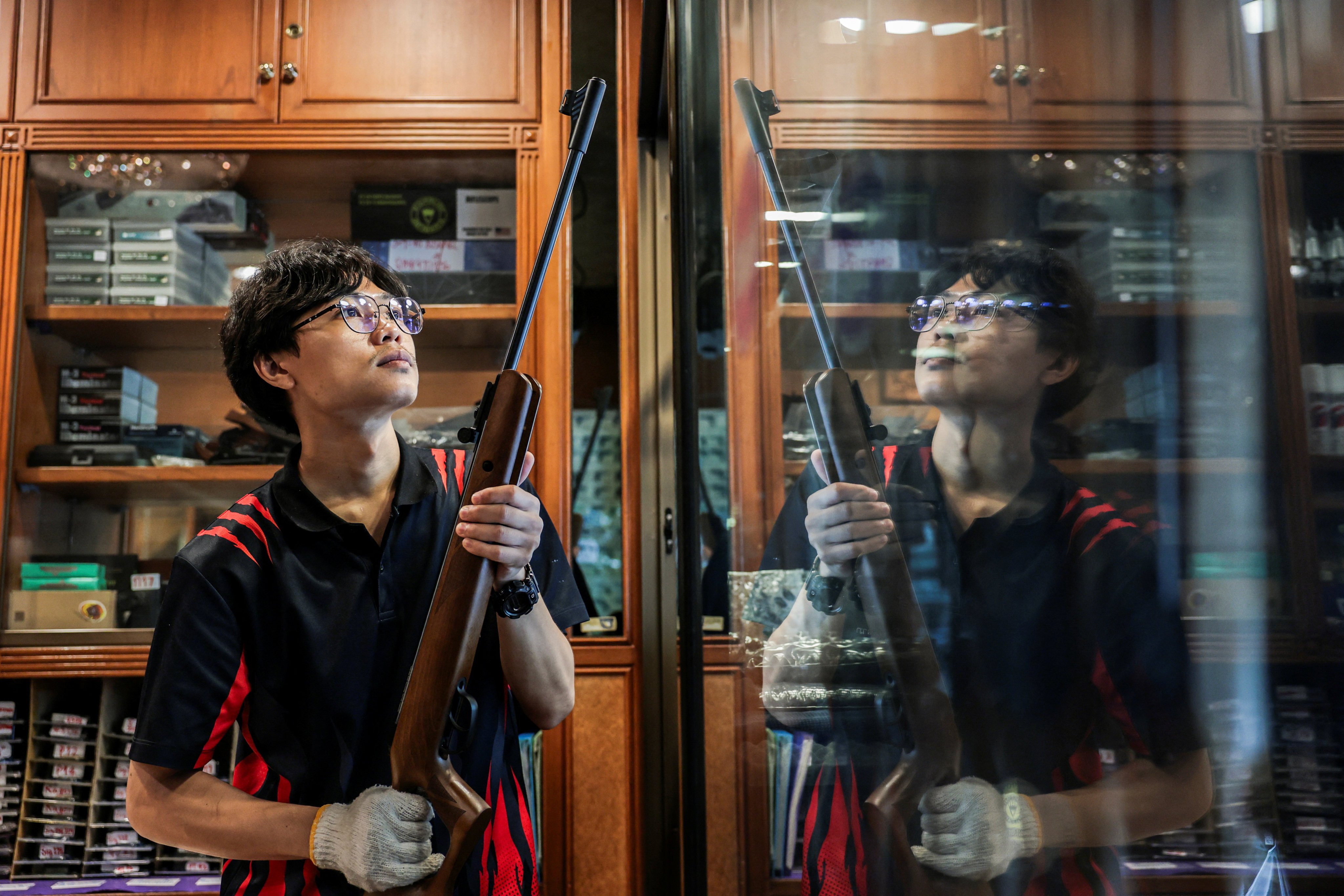 Gun shop worker Piyawat Lumlertwittaya places a rifle back on a display shelf on Friday. Photo: Reuters