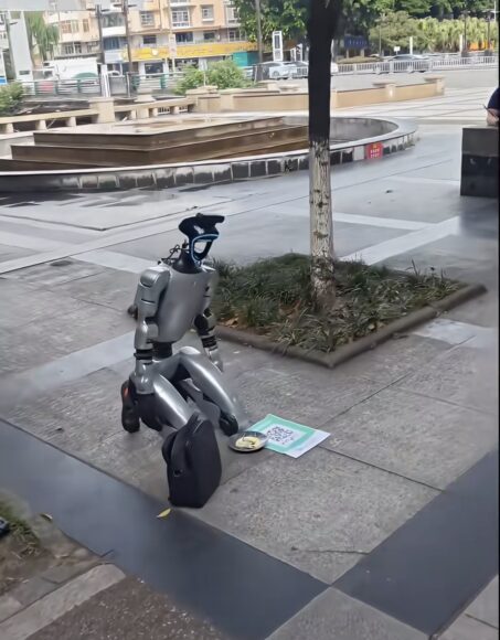 機械人跪地行乞,旁有QR碼和食物.