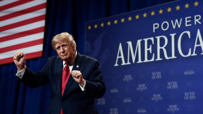 特朗普在演講中揮手,背景是美國國旗和Power of America標誌.