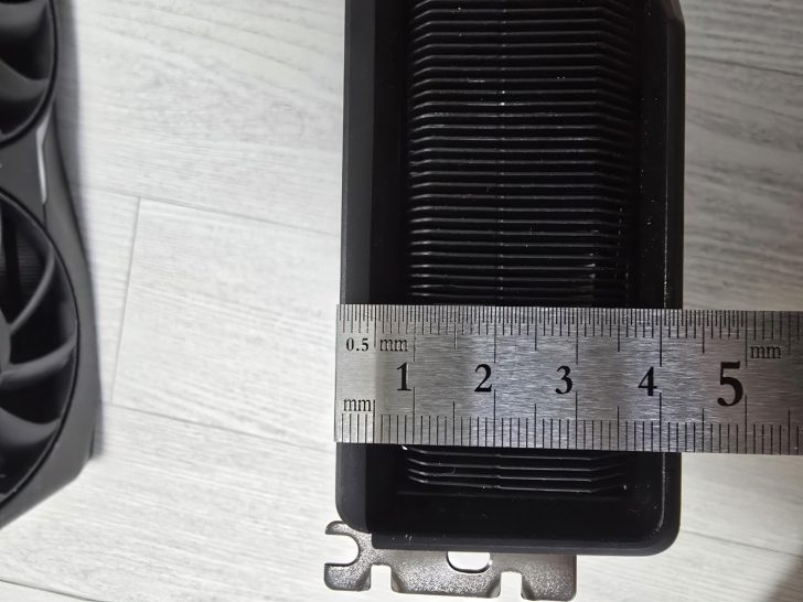 Ruler measuring graphics card heatsink width on a white wooden floor.