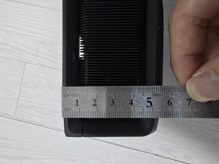 Ruler measuring black object width on wooden surface, hand holding ruler for precise measurement.