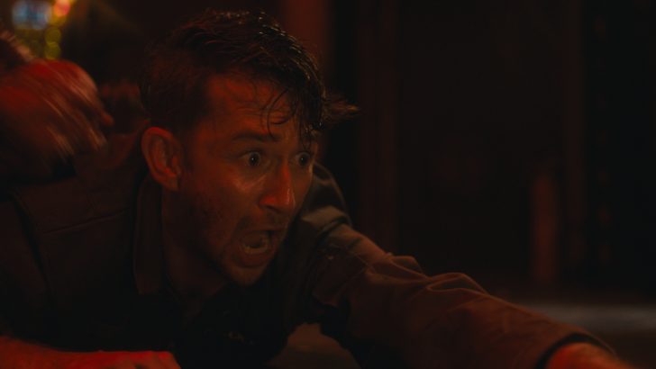 Dead Reset, Man in distress reaching out in a dimly lit scene, expression intense and dramatic.