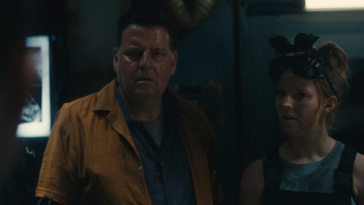 Dead Reset, Two people in a dimly lit industrial setting, one wearing goggles on their head, looking concerned.
