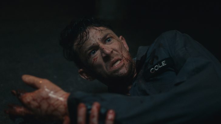 Dead Reset Man with cuts, wearing a uniform labeled Cole, looks distressed and is lying on a dark surface.