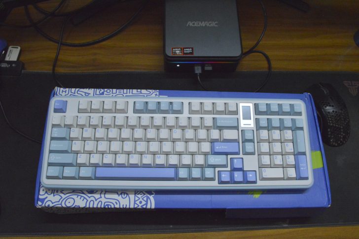 Blue and white mechanical keyboard on a desk, next to a mini PC and gaming mouse.