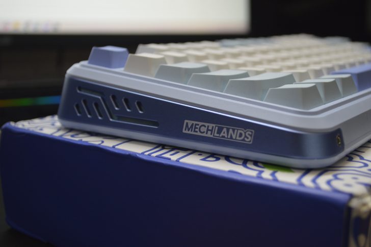 Mechanical keyboard close-up on blue box, showcasing Mechlands branding. Sleek and modern design.