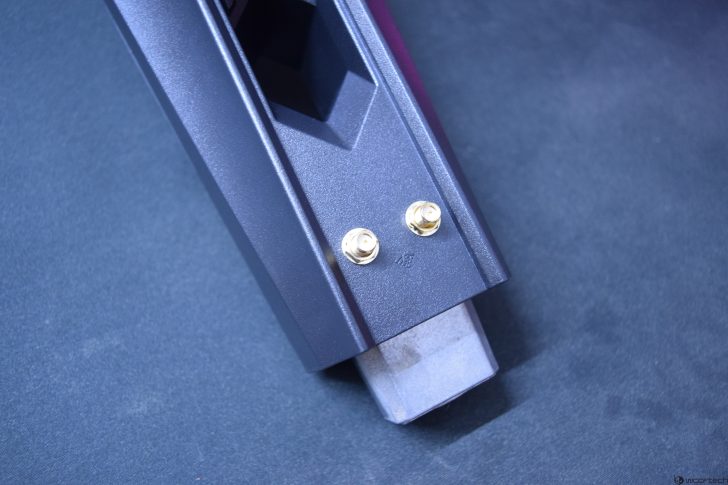 Close-up of a metal component with two gold connectors on a blue background.