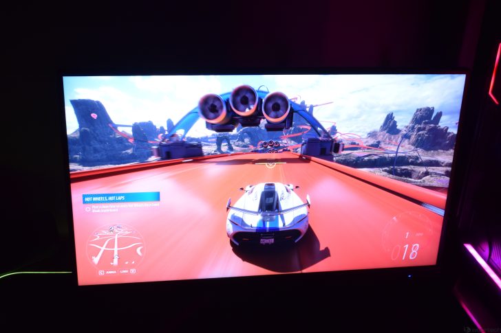 Video game racing scene featuring a futuristic car on a vibrant track within mountainous terrain.
