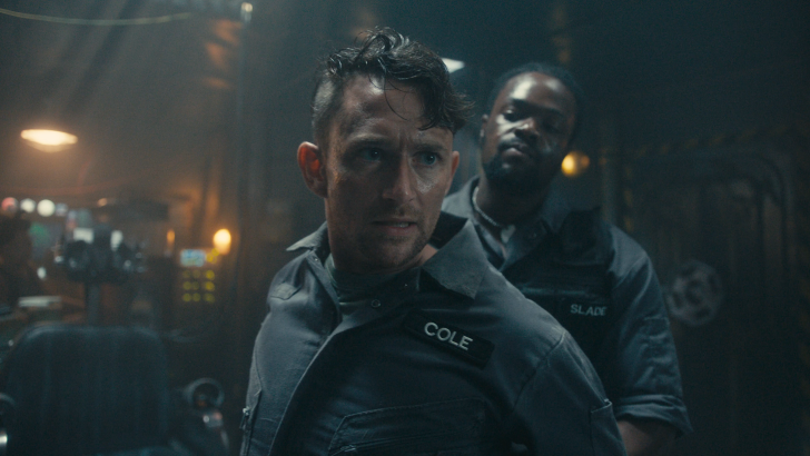 Dead Reset, Two men in dark uniforms standing tensely in a dimly lit room.
