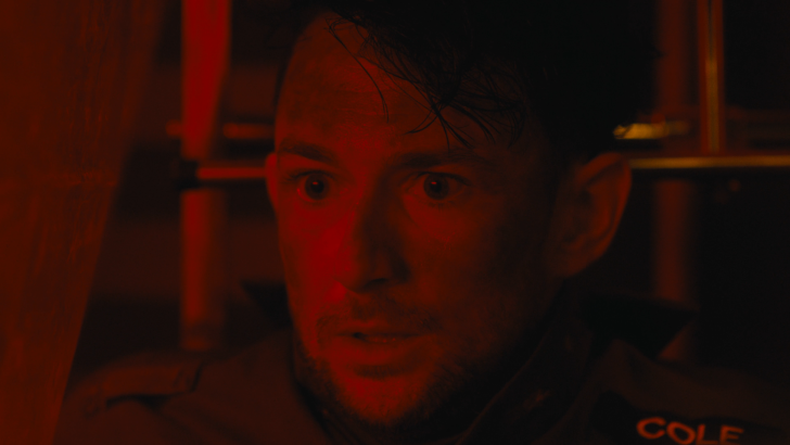 Dead Reset, Tense man in dramatic red lighting, wearing a jacket with Cole on it, showcasing intense expression.