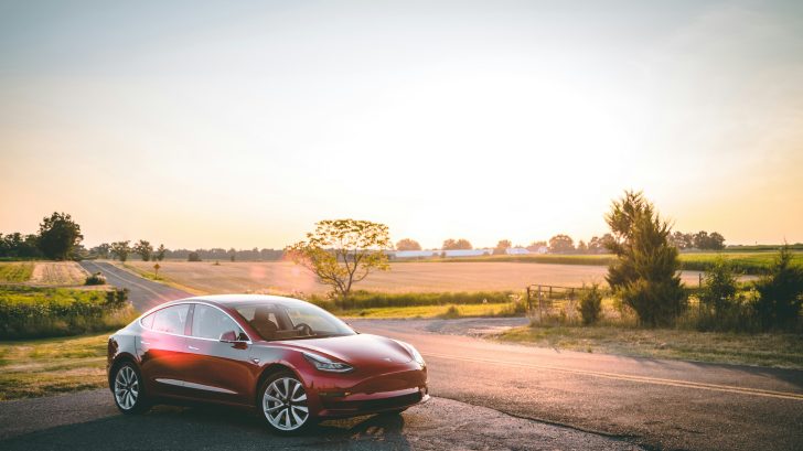 Red electric car on countryside road at sunset.
