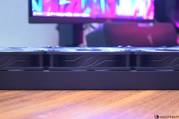 Close-up of black computer hardware on a wooden desk with a colorful monitor background.