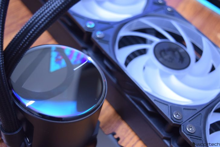 PC water cooling system with black pump, braided cables, and dual fan radiator on wooden surface.