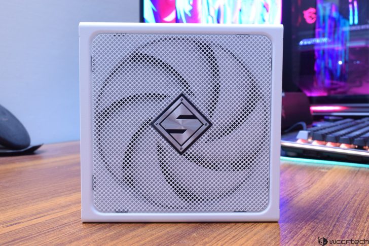 White PC power supply with fan grid on a wooden desk, RGB lights in background.