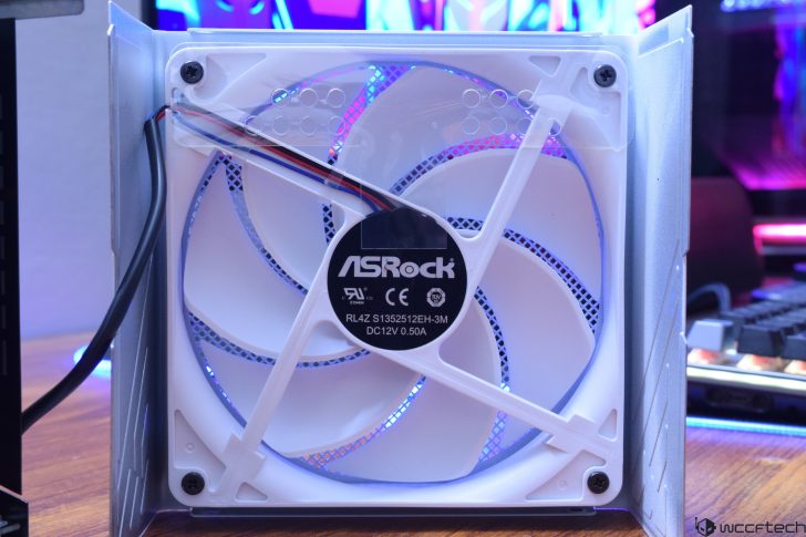 ASRock white PC fan with LED lighting, attached to a computer case on a wooden desk.