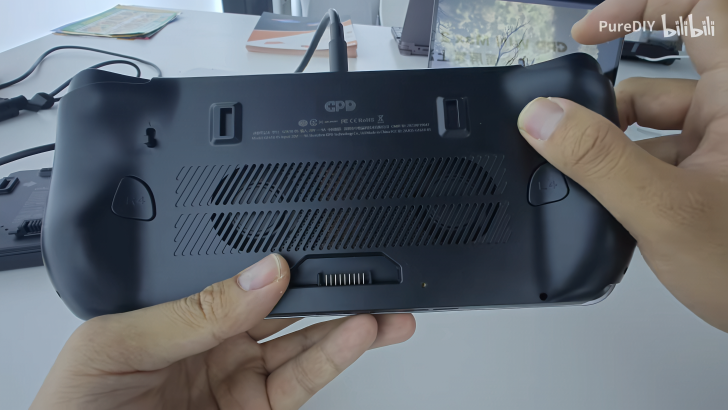 Hand holding a GPD gaming device, showcasing back panel details and buttons.