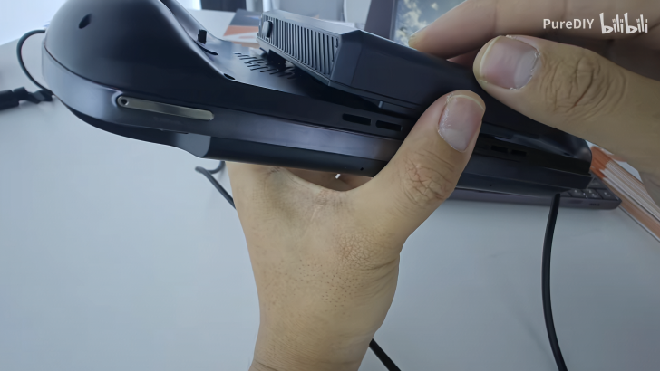 Man holding a portable gaming device with a disk slot, close-up view.