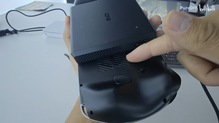 Hand holding a device with visible air vents and buttons, pointing at details on the device.