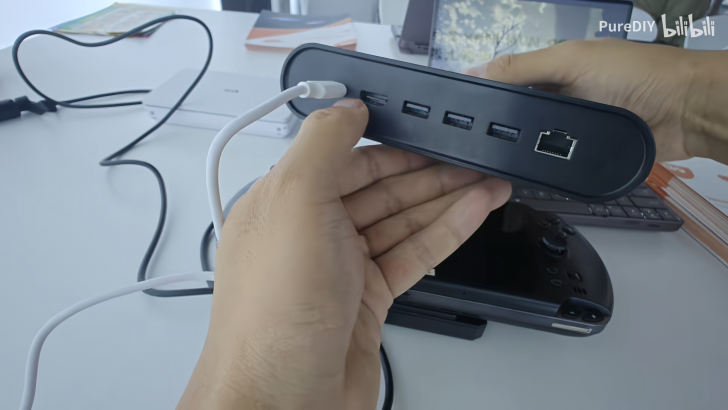 Man holding a USB docking station with multiple ports on a desk.