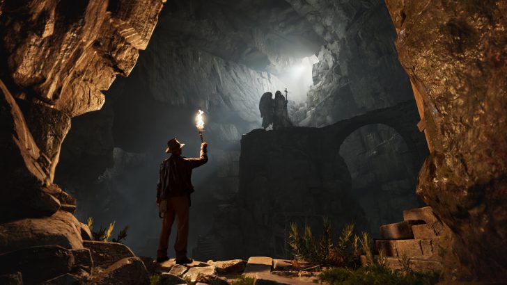 Explorer in cave with torch gazes at angel statue on rock bridge, light streaming from above.