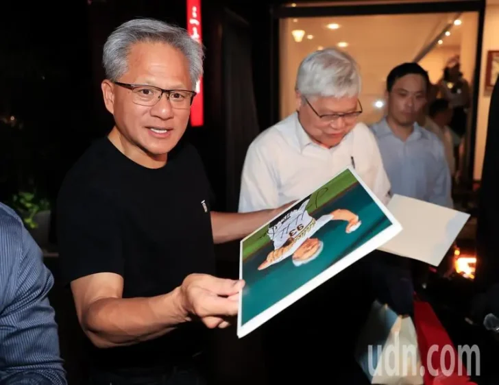 Man holding a signed photo alongside two others in a well-lit room.