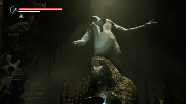 A statue in a cave setting with on-screen text “SWITCH WEAPON” and “SHEATHE WEAPON” at the bottom left.