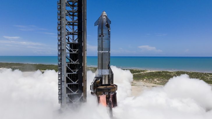 Starship rocket test from seaside platform with smoke and blue sky background.