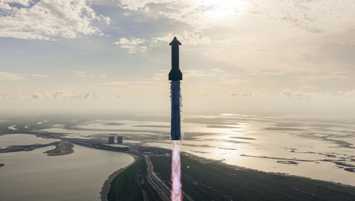 Rocket launches into the sky over a coastal landscape at sunrise.