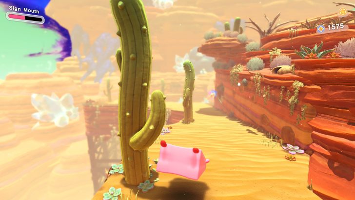Desert scene in video game with cacti, cliffs, and whimsical pink character on sandy path.