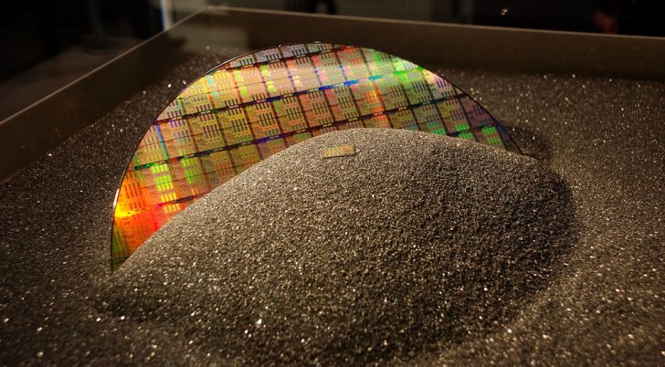 Colorful silicon wafer displayed on glittery black surface.